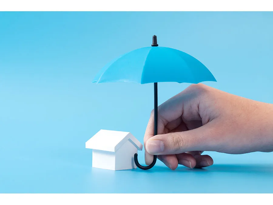 A hand holding a small umbrella over a miniature house
