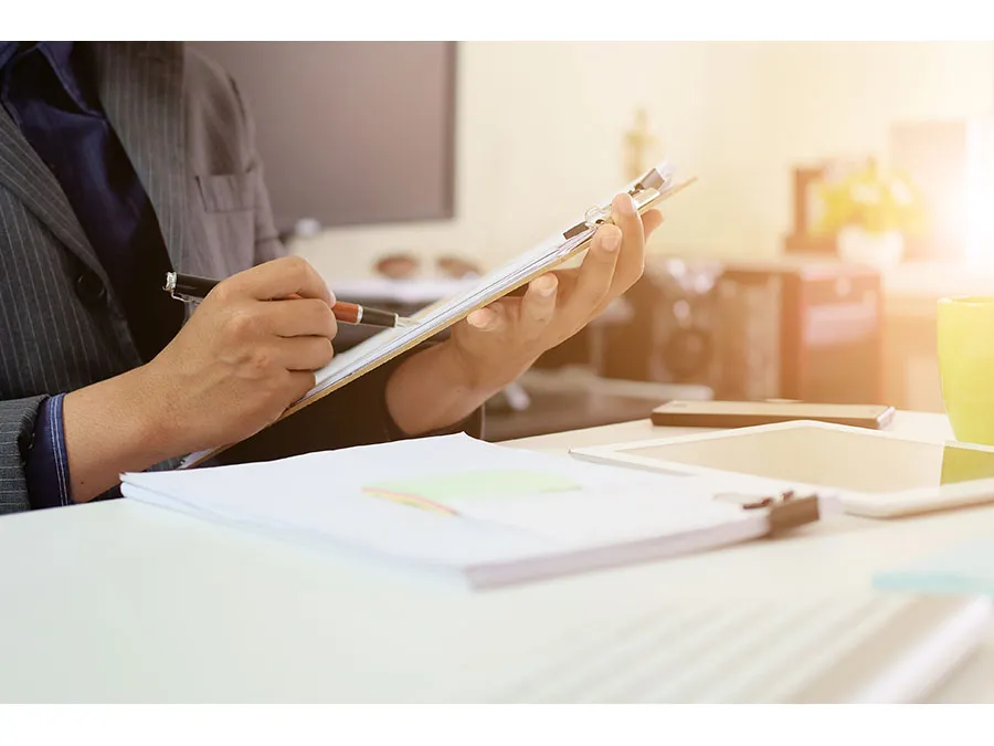 A businessperson reviewing a clipboard of paperwork at a desk