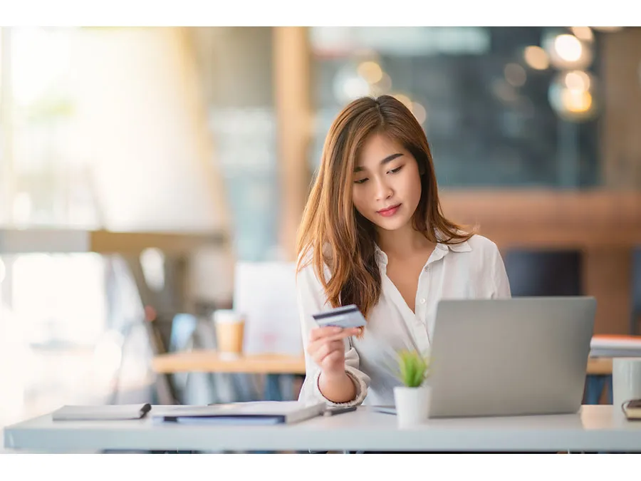 A woman checking a credit card in one hand while looking at a laptop